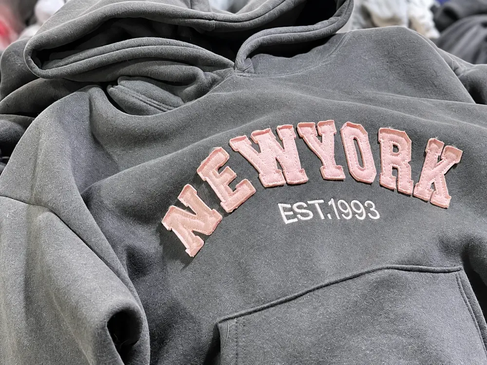 Close-up of pink appliqué lettering on a charcoal washed hoodie
